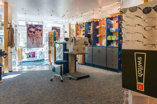 Modernes Optiker-Geschäft mit Brillenregalen, Sehtestgerät und heller Ladeneinrichtung.